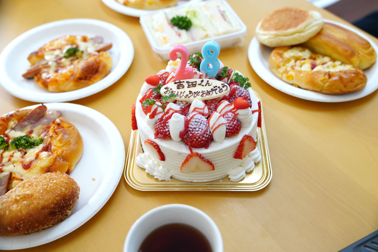中央には誕生日ケーキが置かれており、周りには美味しそうなパンが並べられています